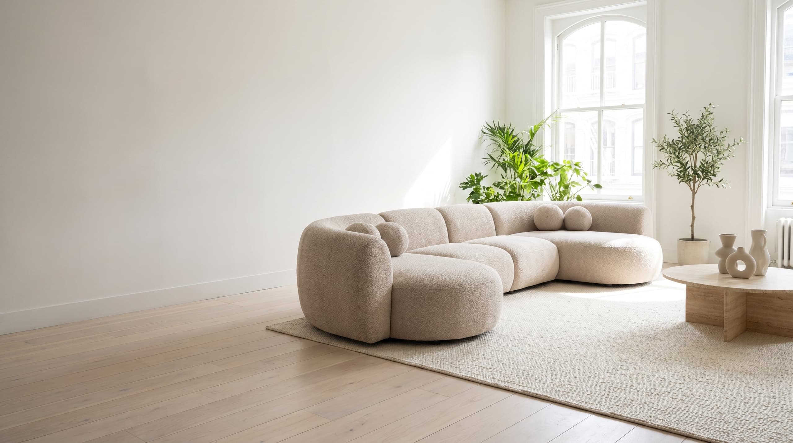 A modern curved modular sectional in ivory bouclé in a bright, sunlit living room